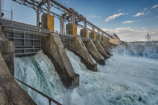 A large hydroelectric dam releases water through gates into a churning river. 