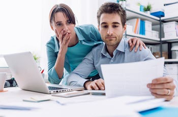 A concerned couple reviews paperwork, possibly about their business. 