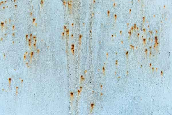 A close-up of a light blue painted metal surface has many scattered rust spots, suggesting corrosion. 