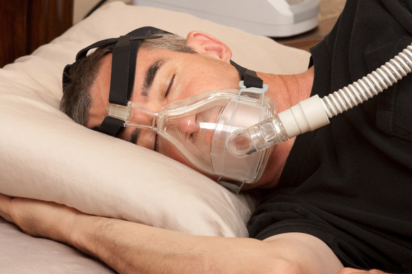 A man sleeps with a CPAP mask connected to a hose. 