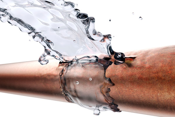 A copper pipe with a hole is gushing water against a white background. 