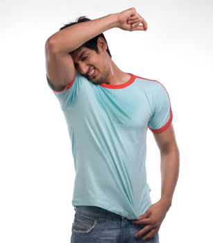 A man wearing a saturated blue t-shirt and blue jeans grimaces while lifting an arm and looking down at his armpit. 