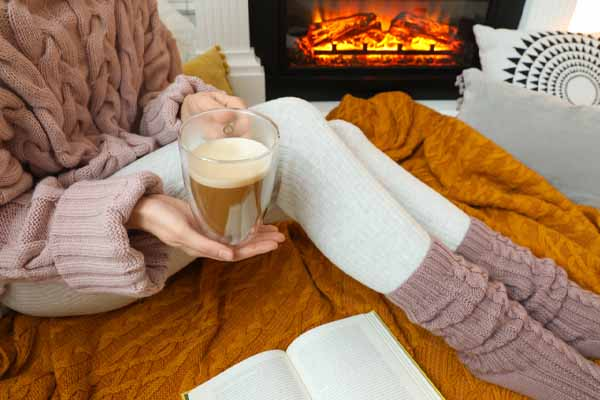 A cozy image shows someone in a sweater, leg warmers, and holding a warm drink. 