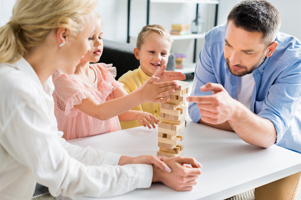 A family of four plays a Jenga game together around a white table. 