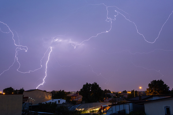 A nighttime photo shows lightning illuminating the sky above a residential area.