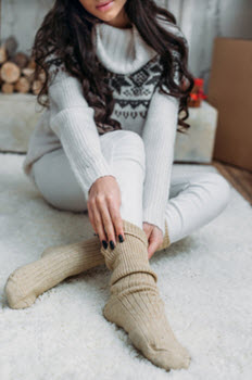 A woman wearing cozy clothing adjusts her knit socks.