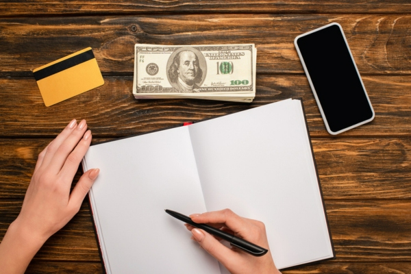 Cropped view of woman about to write on a notebook with cash and card in front of her depicting HVAC cost considerations