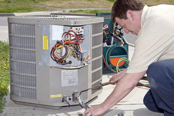 A technician is repairing an HVAC unit, his tools next to him.