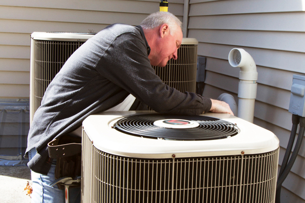 A technician is inspecting an air conditioning unit in front of a house.