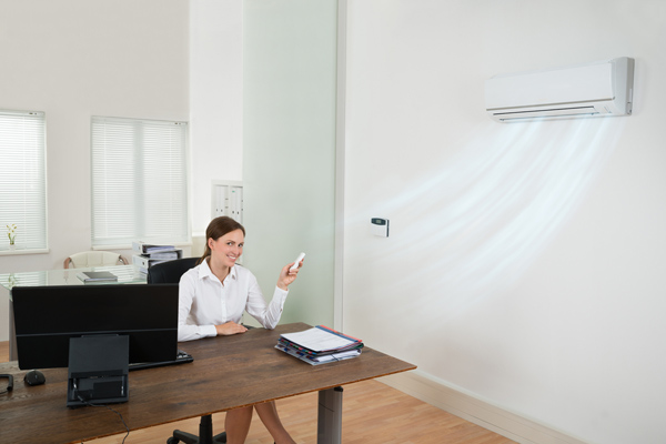 A woman smiles while adjusting her office AC with a remote. 