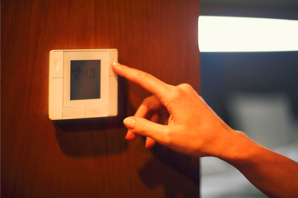 A hand adjusts a digital thermostat on a wooden wall, set to 24.0 degrees.