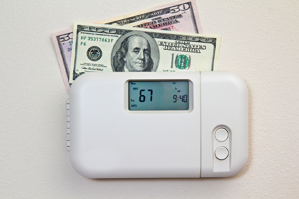 A white thermostat with bills tucked above conveys the concept of heating costs.