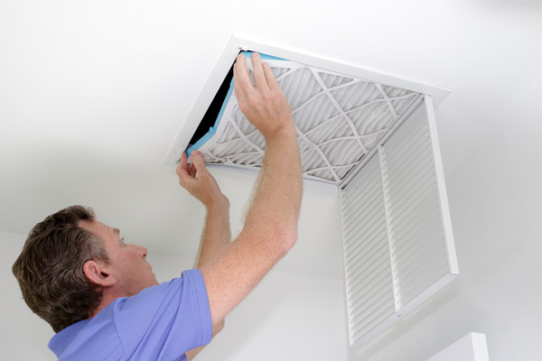 A man replaces an air filter in a ceiling vent.