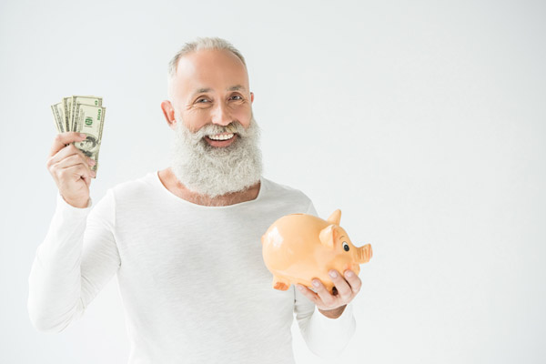 A smiling older man holds cash and a piggy bank against a white backdrop.