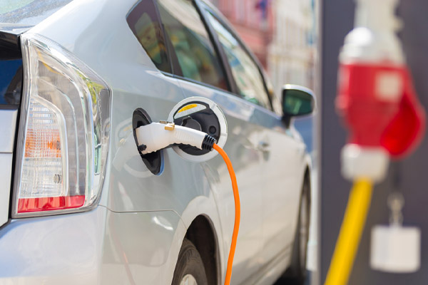 A silver electric car is shown charging at a charging station.