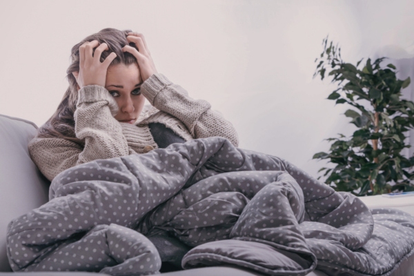 woman sitting on a couch wrapped in a thick blanket depicting heating system breakdown