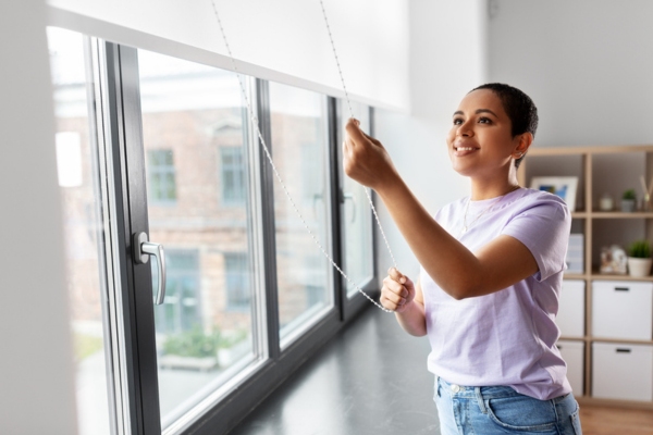woman bringing down window shades to keep cool in summer