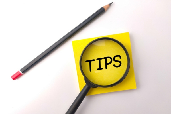 tips written on yellow sticky note viewed by magnifying glass beside a black pencil