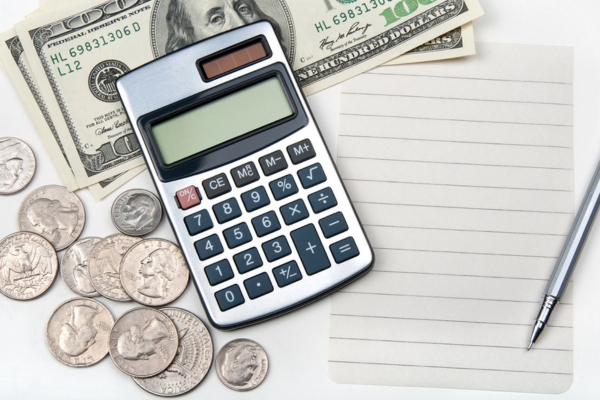 calculator and dollar bills and coins beside an empty paper depicting controlling heating oil expenses